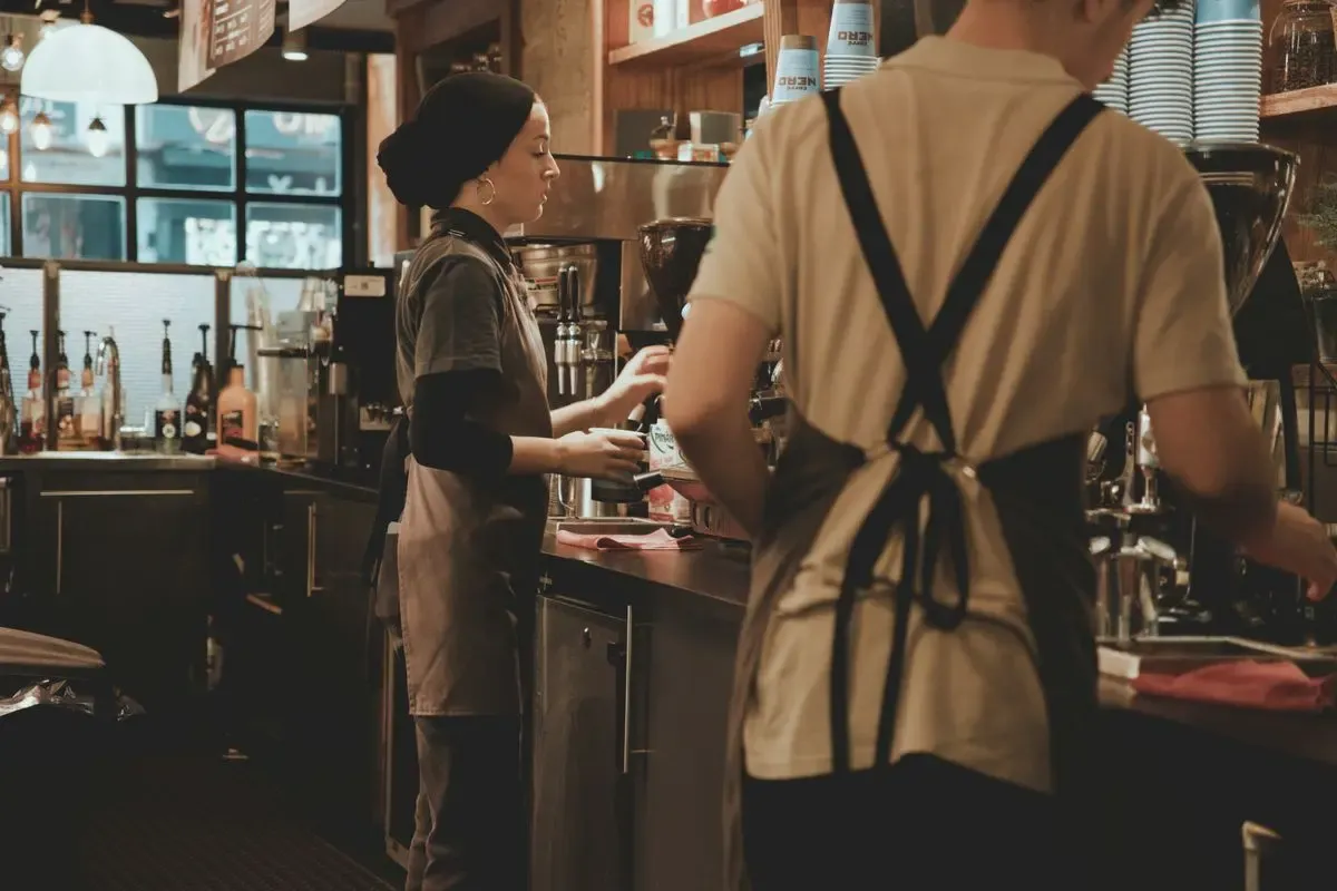Dos baristas de espaldas preparando café detrás de la barra de una cafetería